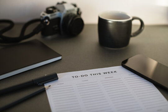 Close-up of a To do list, notebook, pens, mobile phone, camera and a cup of black coffee on a desk