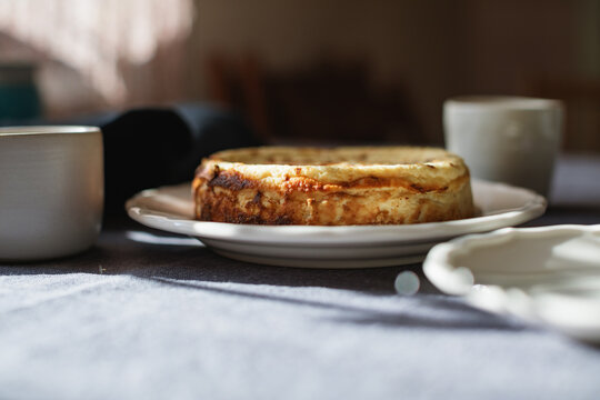 Close-up Side view of a Basque burnt cheesecake on a table with assorted crockery in sunlight