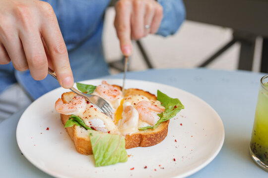 Close-up of man eating a shrimp toast with a poached egg and greens at an outdoor garden table with a refreshing passion fruit and chia drink