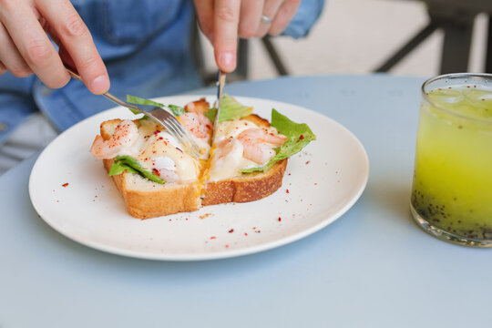 Close-up of man eating a shrimp toast with a poached egg and greens at an outdoor garden table with a refreshing passion fruit and chia drink