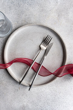 Overhead view of a rustic place setting with a red ribbon on a grey kitchen worktop