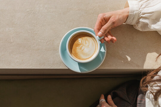 Close-up of a woman sitting at a table holding a cappuccino