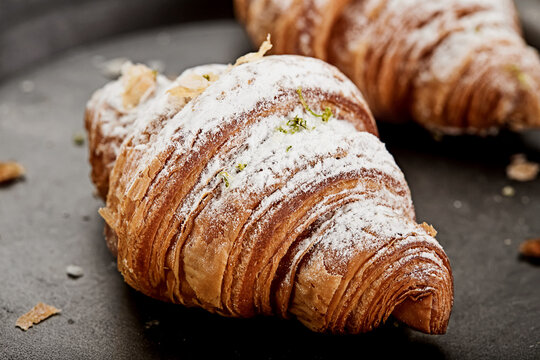 Close-up of two croissants dusted with icing sugar on a metal tray