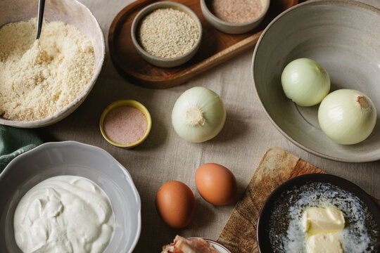 Overhead view of assorted ingredients for making an onion and bacon tart with almond flour on a linen tablecloth