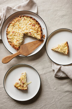 Close-up of a homemade savoury gluten free keto onion and bacon tart with an almond flour crust on a plate with two slices on plates, a cake server and napkins