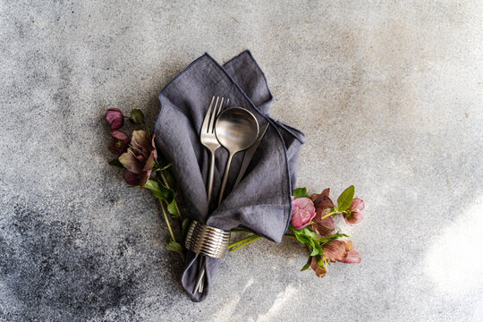 Overhead view of a springtime cutlery setting with fresh purple hellebore (Helleborus orientalis) flowers on a grey background