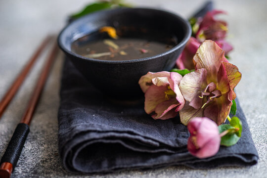 Close-up of a cup of herbal tea on a folded napkin with chopsticks and purple hellebore (Helleborus orientalis) flowers