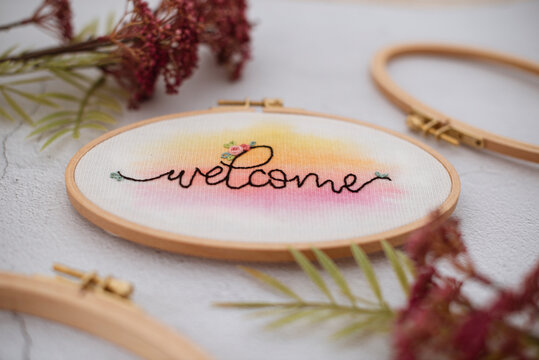 Close up of embroidery hoop with the word welcome on a  table with flowers