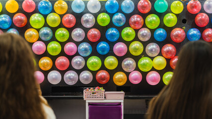 People playing a game at an amusement park or fair, aiming at a wall of vibrant balloons © pablo