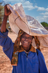 Smiling village African Woman Carrying a Large White Sack on Her Head balancing load © poco_bw
