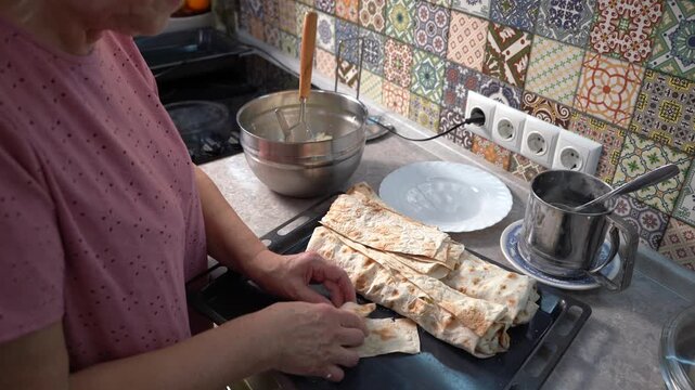 Elderly woman cooking food at home. Make pies. Roll pita cottage cheese dough