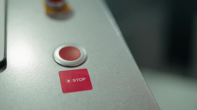 Close-up of a red stop button on a metallic industrial control panel with a focus shift revealing a large emergency push button in the background, symbolizing safety and production control