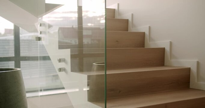 Modern and minimalist staircase with wooden steps and a glass balustrade, revealing a clean, bright, and luxurious home interior design with a large potted plant next to a window