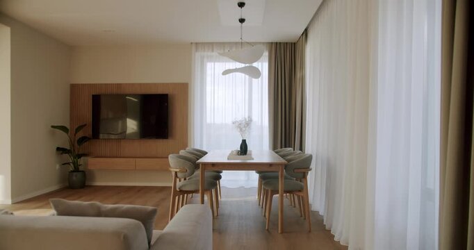 Luxurious living room featuring a modern minimalist design with a dining area, wooden table, comfortable chairs, and a large window with sheer curtains, all bathed in warm, natural sunlight