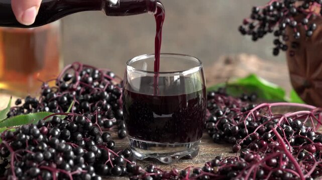 Hand Pouring black elderberry syrup from a bottle into a glass on a table