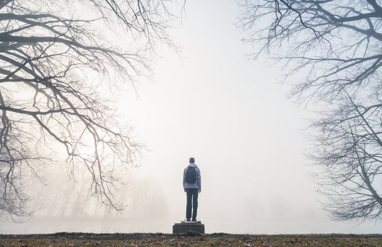 Man from back standing on flood gate on pond shore with mystery fog and tree branches. Czech landscape background
