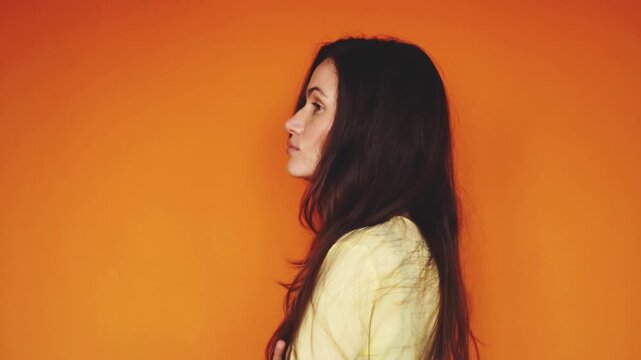 Horizontal video of arrogant brunette woman turning away with disdain on orange background. Haughty girl with crossed arms looking aside and showing indifference. Superiority and rejection concept