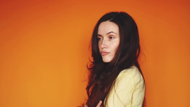 Horizontal video of arrogant brunette woman standing in profile and looking over shoulder with disdain. Haughty girl with crossed arms showing indifference on orange background. Superiority concept