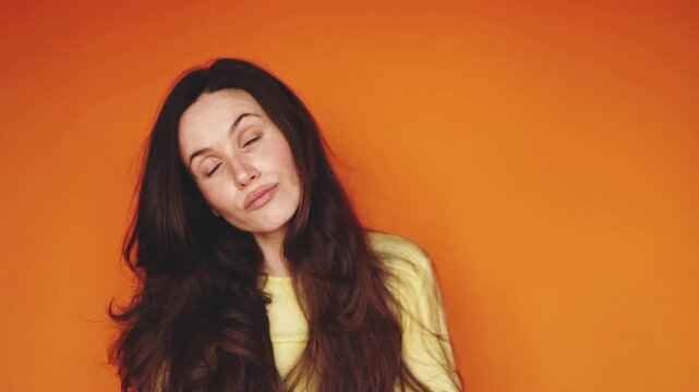 Horizontal video of skeptical brunette woman looking at camera with disdain on orange background. Haughty girl tilting head and pouting lips, showing superiority and boredom. Cynical emotion