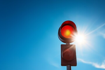 Naklejka premium Red traffic light illuminated against a clear blue sky, with a sunburst creating flares