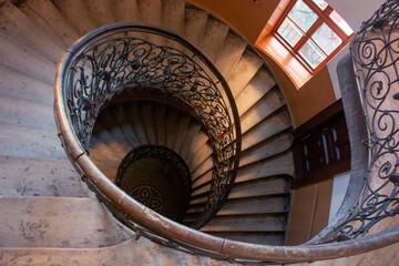 Fototapeta premium Elegant spiral staircase ornate wrought iron railing stone steps illuminated natural light window.