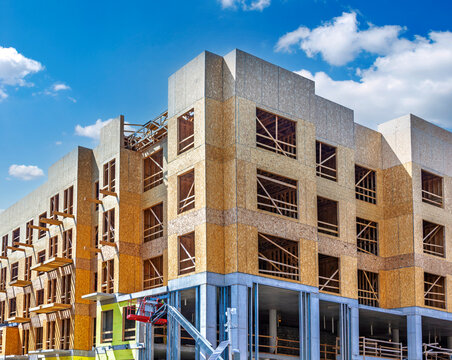 Multi-story residential building under construction using wood frame and OSB sheathing on a concrete podium base.