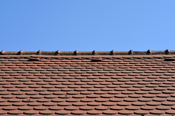 Naklejka premium A wide shot of a classic red clay shingle roof featuring a repetitive scale pattern against a bright and clear blue sky background.