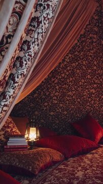 Cozy bohemian bed nook with lantern, patterned drapes, plush pillows and stacked books; warm golden glow, textured wallpaper, velvet cushions, intimate evening atmosphere ideal for reading