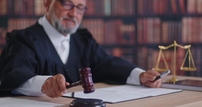 Judge holding gavel delivering verdict of law and justice due court process. Senior magistrate wearing robe, giving judgment decision, sitting with legal documents and scales in formal courtroom