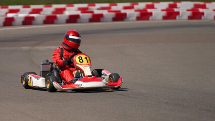 Children's karting. A child in red protective clothing and a protective helmet turns a racing car around a track.