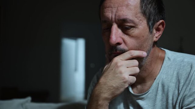 Low key portrait of mature adult man rethinking in dark room under warm soft light, introspective mood. 4K.