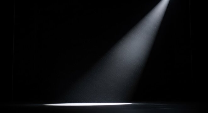 Single bright spotlight illuminates an empty dark stage floor, creating a dramatic focus beam of light.