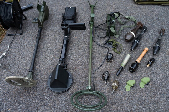 Professional metal detectors and various deactivated grenades and mortar shells laid out on a gray surface for display or training.
