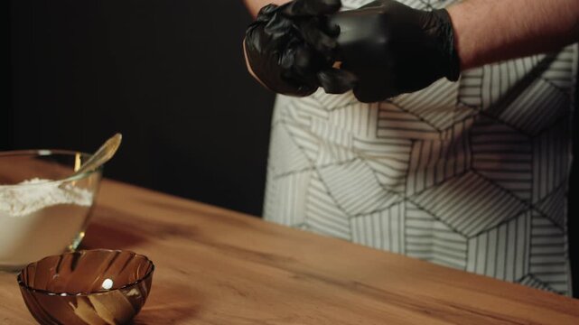 Caucasian man wearing patterned apron pulls on black gloves. Closeup of male hands and preparation for cooking in kitchen. Maintaining hygiene and sanitation while cooking and baking