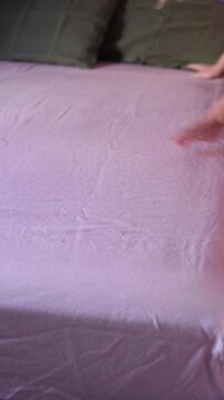 female hands making the bed with dusty pink linen sheets