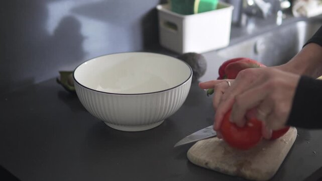 A woman washes fresh tomatoes and cuts them on a kitchen cutting board to prepare a homemade vegetable salad. Close-up of hands slicing ripe tomatoes in a modern home kitchen