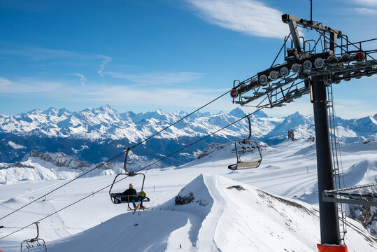 Alps, Europe - 09.02.2026: Skiers riding chairlift over snowy mountain slopes under blue sky