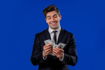 Happy excited businessman counts cash money - USD currency dollars banknotes on blue. Symbol of jackpot, gain, victory, winning the lottery