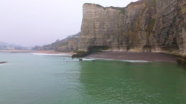 Aerial tracking shot of limestone cliffs and rocky shoreline receding into misty bay at overcast morning