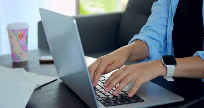 Focused typing activity. Individual diligently working at desk with coffee and smartwatch visible. Person concentrated on typing at workstation accompanied by coffee and nearby wristwatch