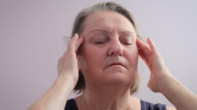 An elderly woman massages her temples to relieve a headache.