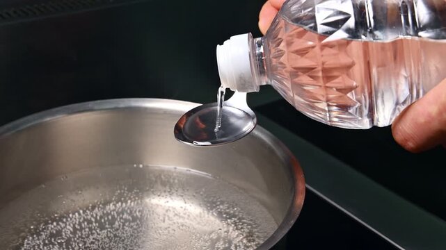 Pouring vinegar from bottle into spoon above boiling pot of water