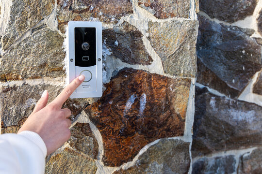 Hand Pressing Video Doorbell on Stone Wall. Close-up of a hand pressing a video doorbell on a stone wall, illustrating smart home entry, access control, and security.