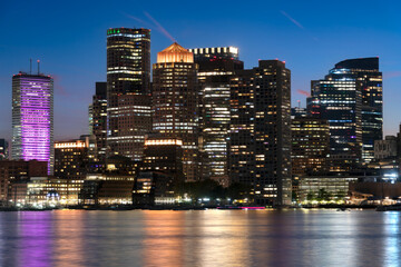 Naklejka premium The illuminated skyscrapers of downtown Boston reflect in the calm waters of the harbor during the blue hour.