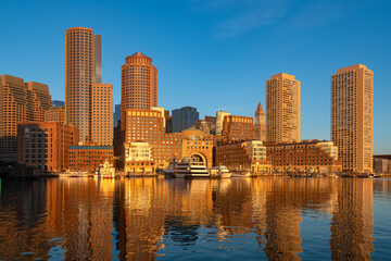Obraz premium The Boston skyline is illuminated by the golden morning light of sunrise over the harbor.