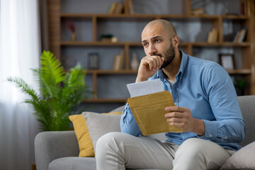 Man feeling anxious and stressed while holding an open envelope with a letter, contemplating...