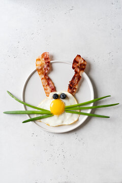 Easter concept with funny fried egg bunny and becon on plate on white background, top view