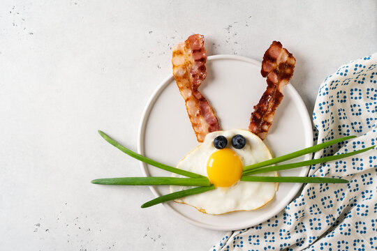 Easter concept with funny fried egg bunny and becon on plate on white background, top view