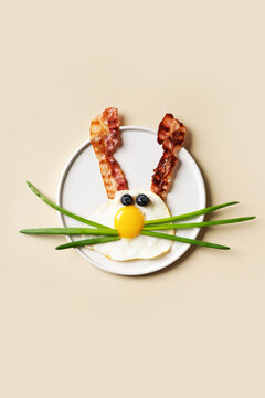 Easter concept with funny fried egg bunny and becon on plate on beige background, top view