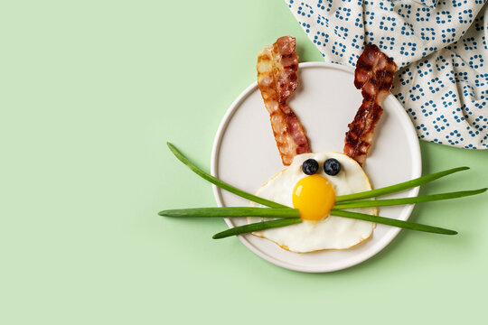Easter concept with funny fried egg bunny and becon on plate on white background, top view